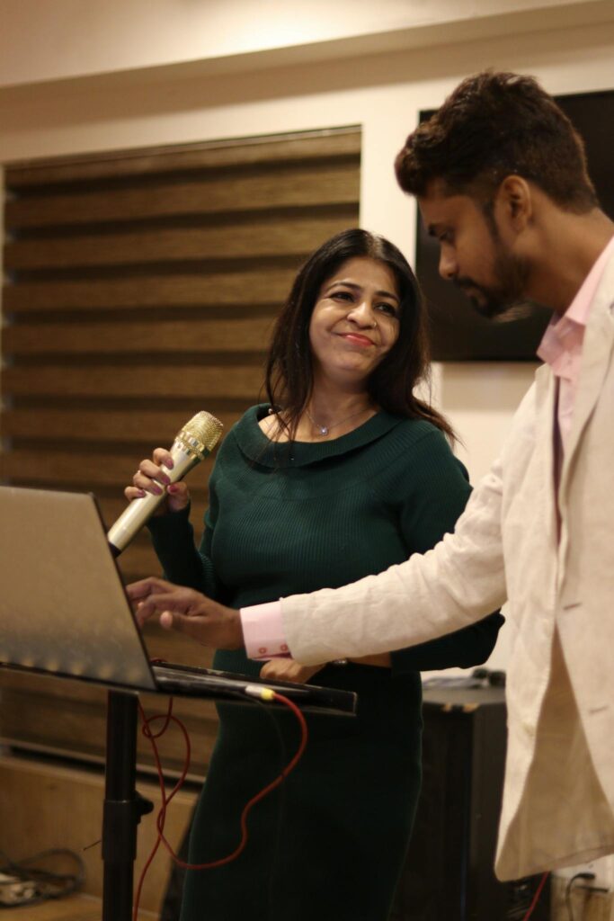 A businesswoman using a microphone during a presentation while a colleague assists at a laptop.