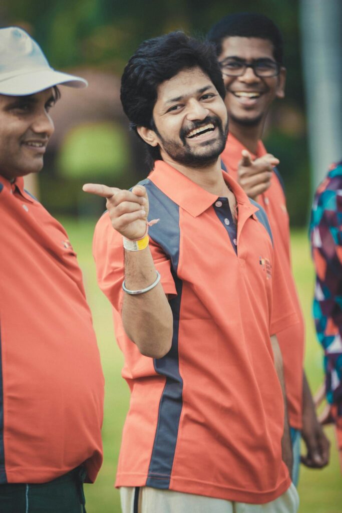 Group of cheerful men in orange jerseys pointing and smiling outdoors, enjoying a fun moment.