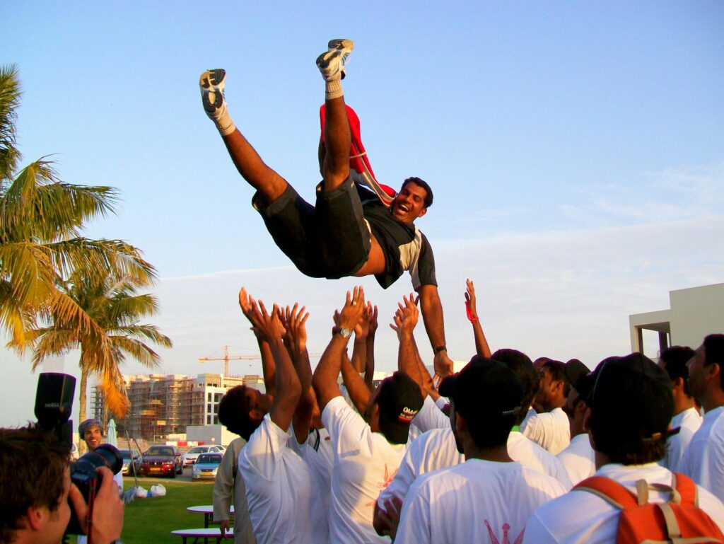 Joyful celebration with a teammate being tossed in the air during a sailing event in Oman.